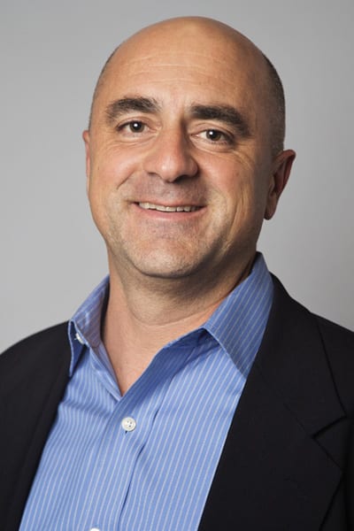 A man in a suit and blue shirt smiling.